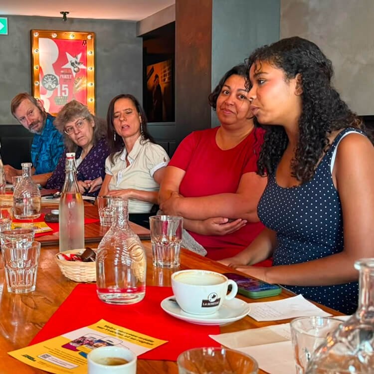 Cinq participants assis côte à côte autour d’une table écoutent une jeune femme prendre la parole.