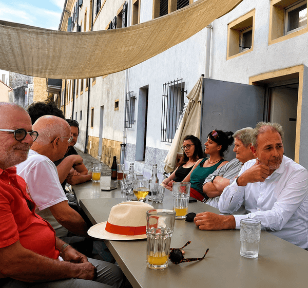 Une longue tablée en terrasse, au pied d’un immeuble aux encadrements jaunes : les participants discutent autour de verres de jus.