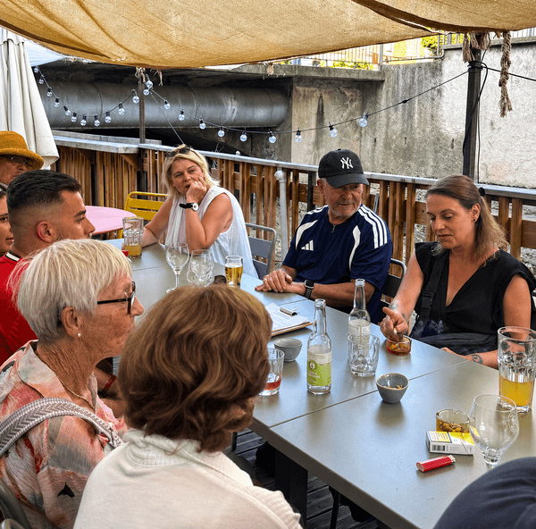 Sous une guirlande lumineuse, une participante écoute, la main au menton, pendant que la discussion se poursuit autour de la table.